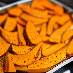 a tray of butternut squash wedges, olive oil, harissa, black pepper, and 1 tsp salt that are well blended.