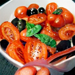 a bowl containing olive oil, torn basil, black olives, halved cherry tomatoes, drained capers, lemon zest and lemon juice.