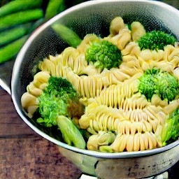 the cooked pasta and veggies are drained in a colander.