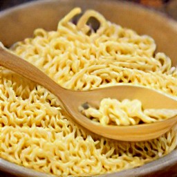 the egg noodles are transferred to a large bowl and drizzled with 3 tbsp of sesame oil. they are then stirred with a wooden spoon for 2 minutes.